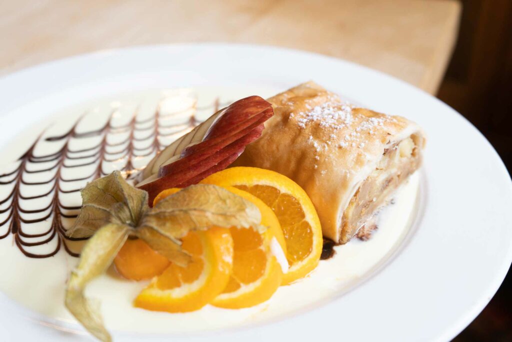 Fein angerichtetes Stück Apfelstrudel mit Vanillesoße und Orangenscheiben