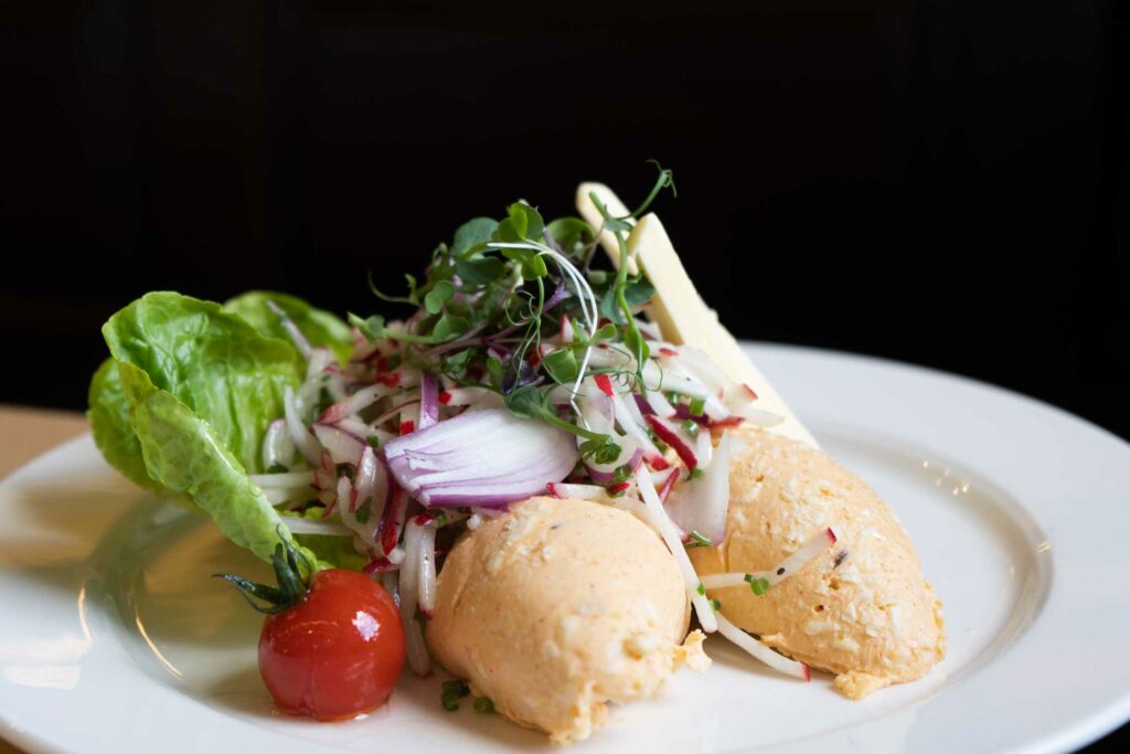 Obazda mit frischem Blattsalat, Radieschen und Tomaten wird auf einem weißen Teller serviert.