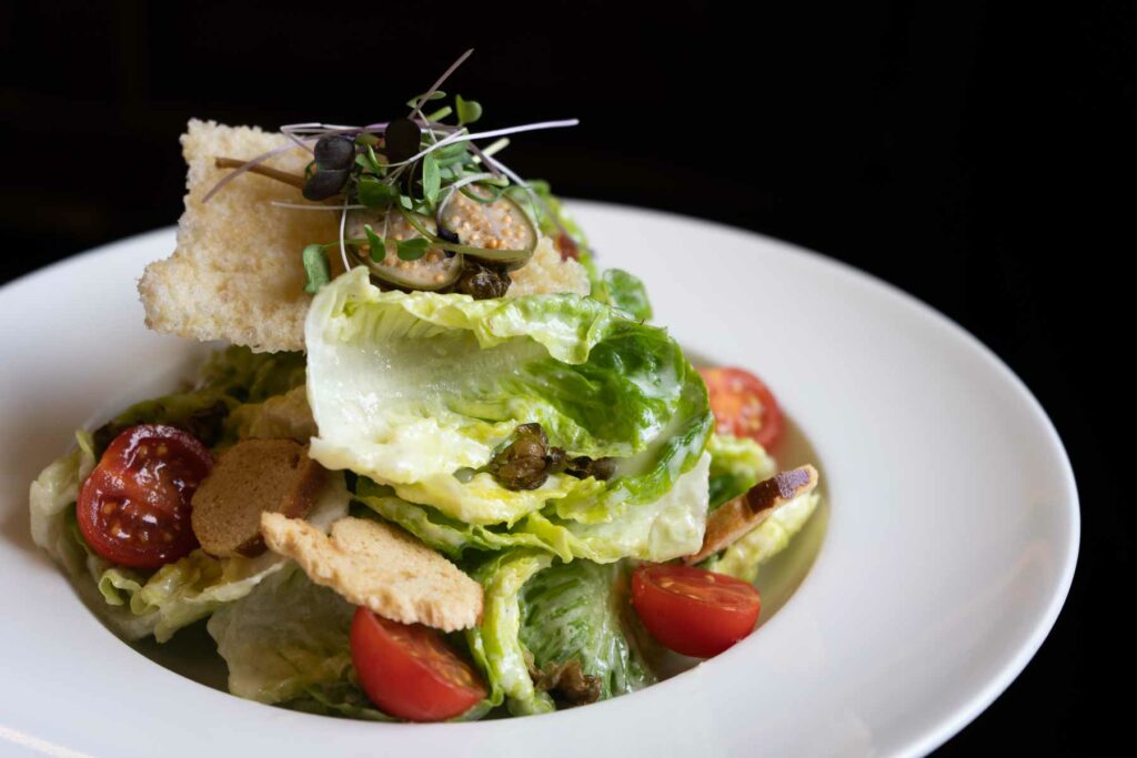 Ein rustikaler Salat mit Brotstücken, Tomaten, Blattsalat und gebratenem Fleisch ist dekorativ angerichtet.