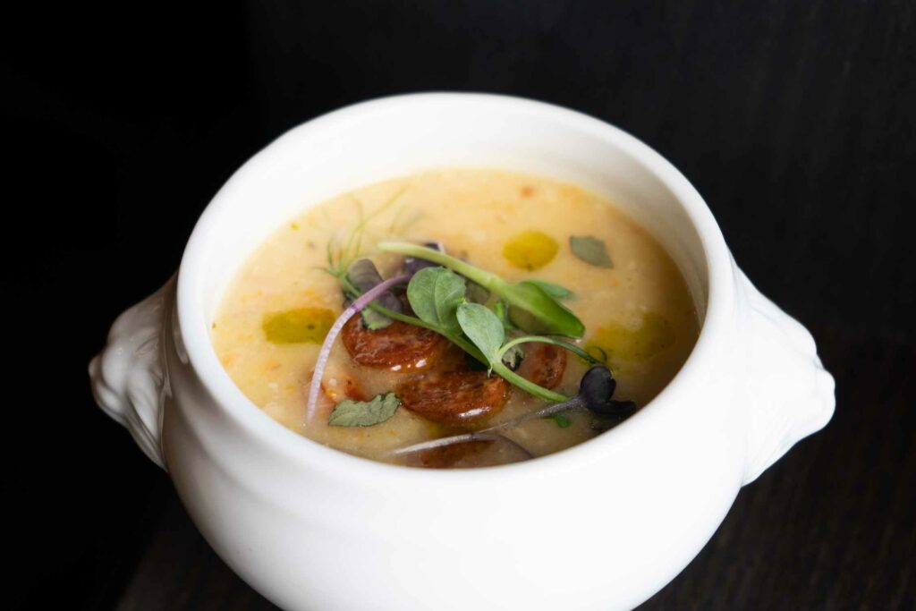 Cremige Suppe mit Gemüse, Kräutern und feiner Einlage wird in einer weißen Suppenschale.