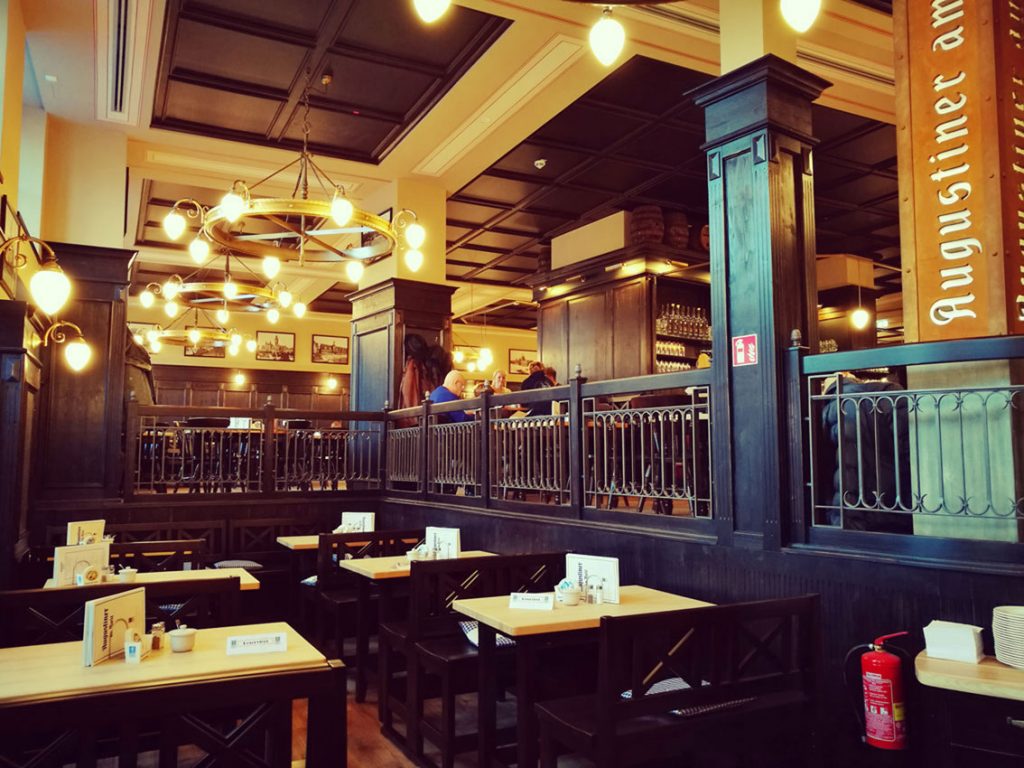 Ein offen gestalteter Restaurantbereich mit Holzgeländern, klassischen Leuchten und mehreren Tischgruppen.