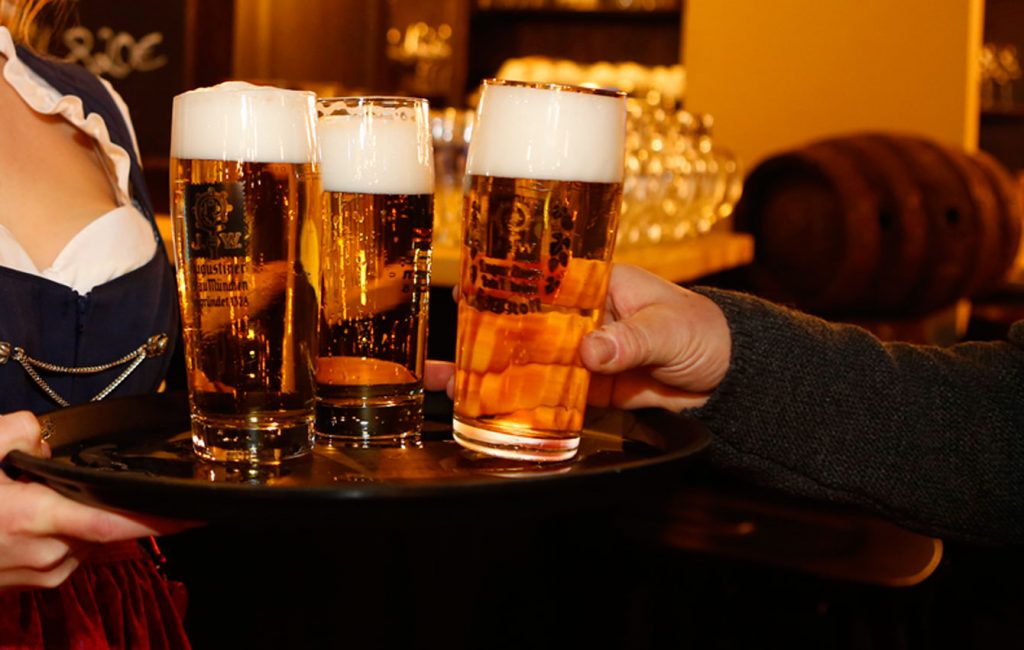 Drei goldgelbe Augustiner-Biere mit kräftiger Schaumkrone werden auf einem Tablett serviert.
