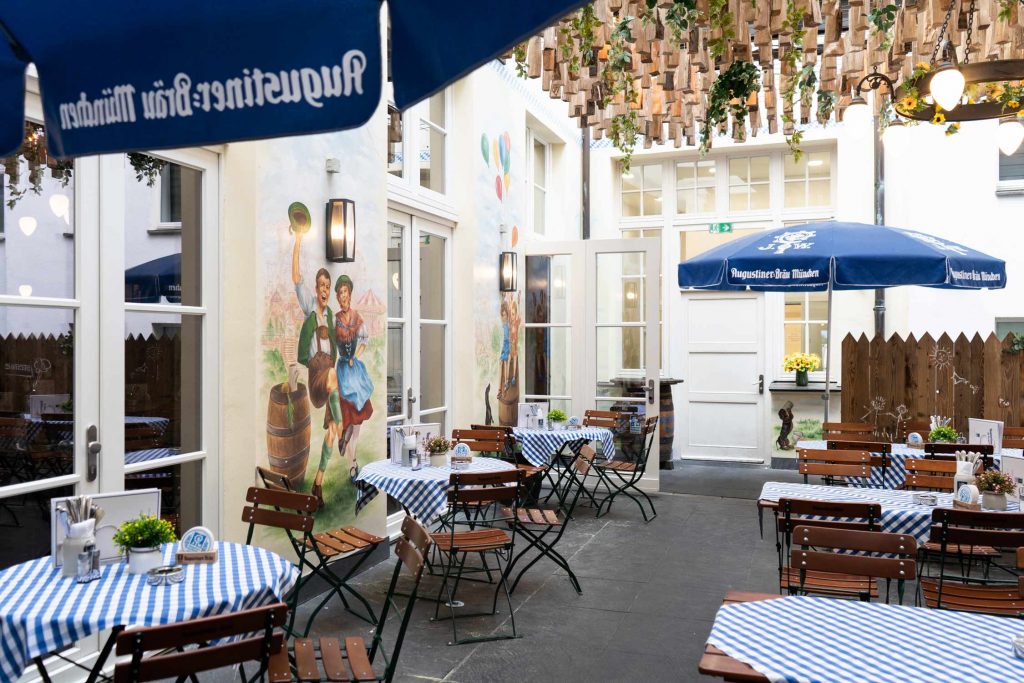 Unter blauen Sonnenschirmen laden gedeckte Tische und rustikale Sitzmöbel zum entspannten Verweilen ein.