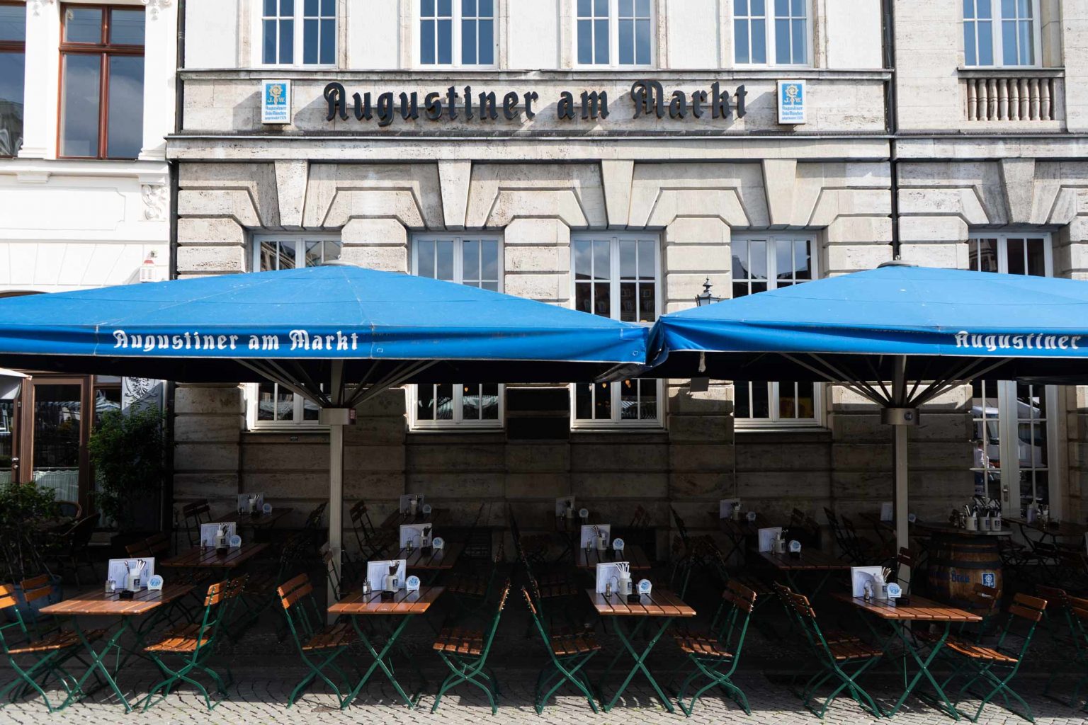 Die historische Fassade mit blauen Markisen und großzügigem Außenbereich zeigt das Augustiner-Wirtshaus in zentraler Lage.