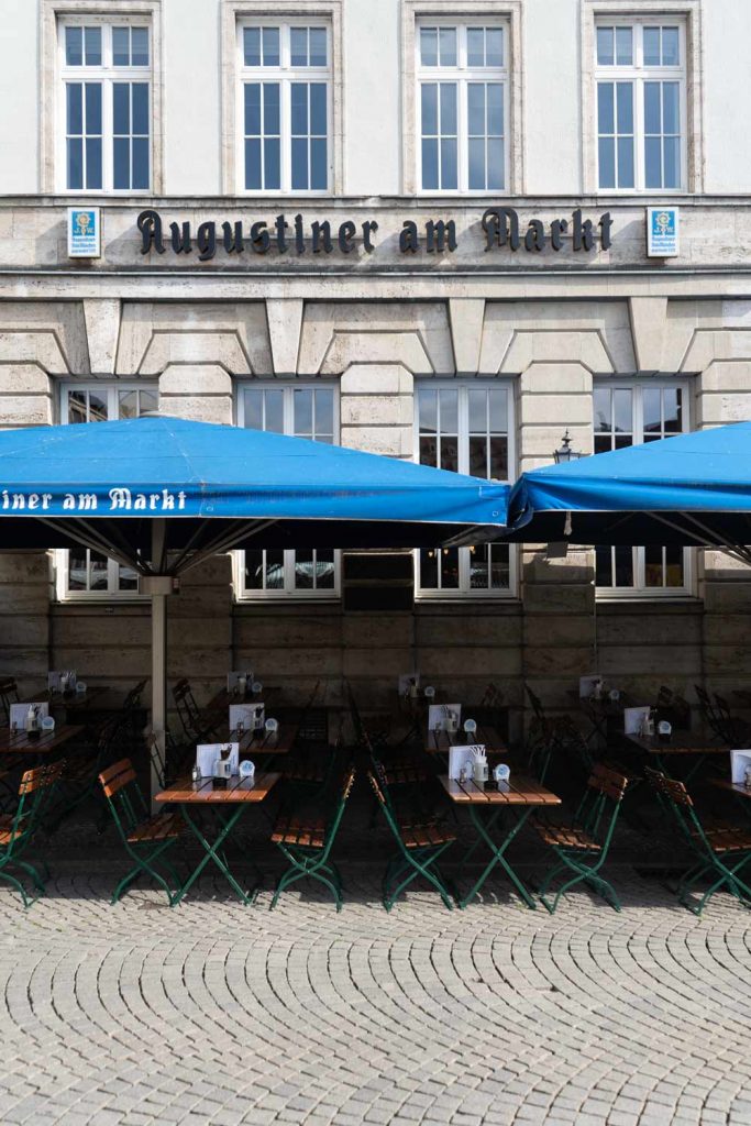 Die Fassade mit blauen Markisen und Außensitzplätzen präsentiert das Augustiner am Markt im Leipziger Zentrum.