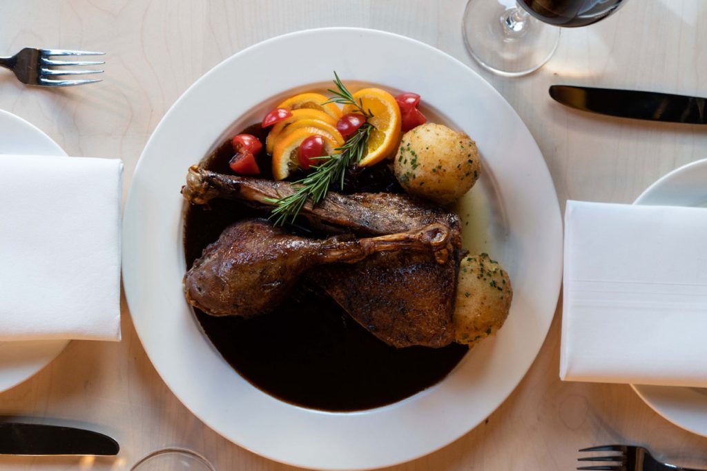 Gebratene Ente mit dunkler Sauce, Kartoffeln, Orange und frischen Kräutern serviert.