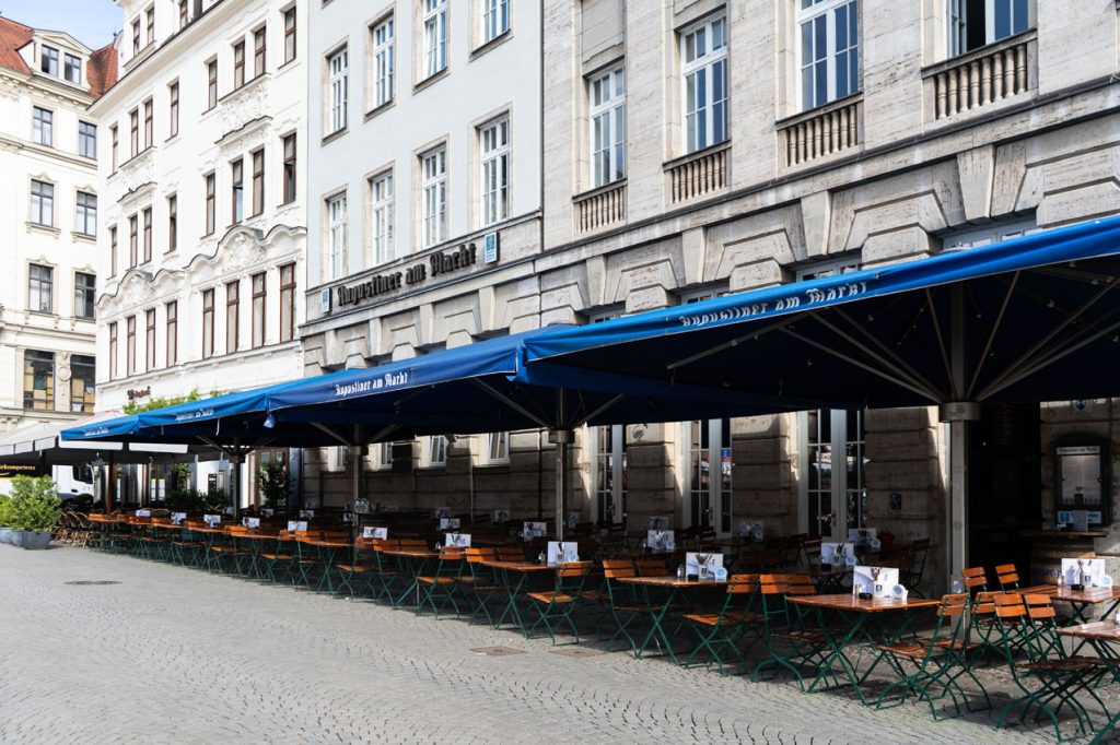 Der langgestreckte Außenbereich mit blauen Augustiner-Markisen bietet zahlreiche Sitzplätze entlang der historischen Fassade.
