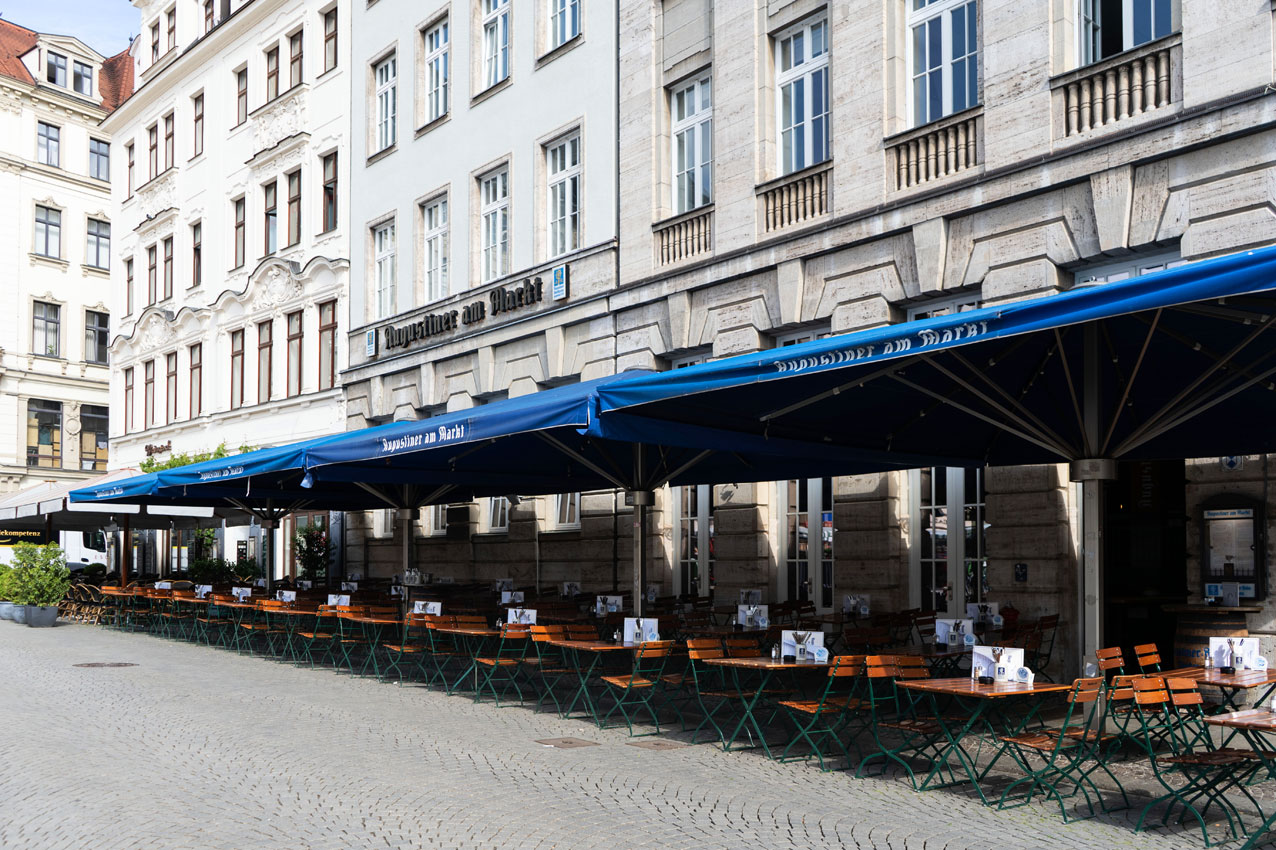Der langgestreckte Außenbereich mit blauen Augustiner-Markisen bietet zahlreiche Sitzplätze entlang der historischen Fassade.
